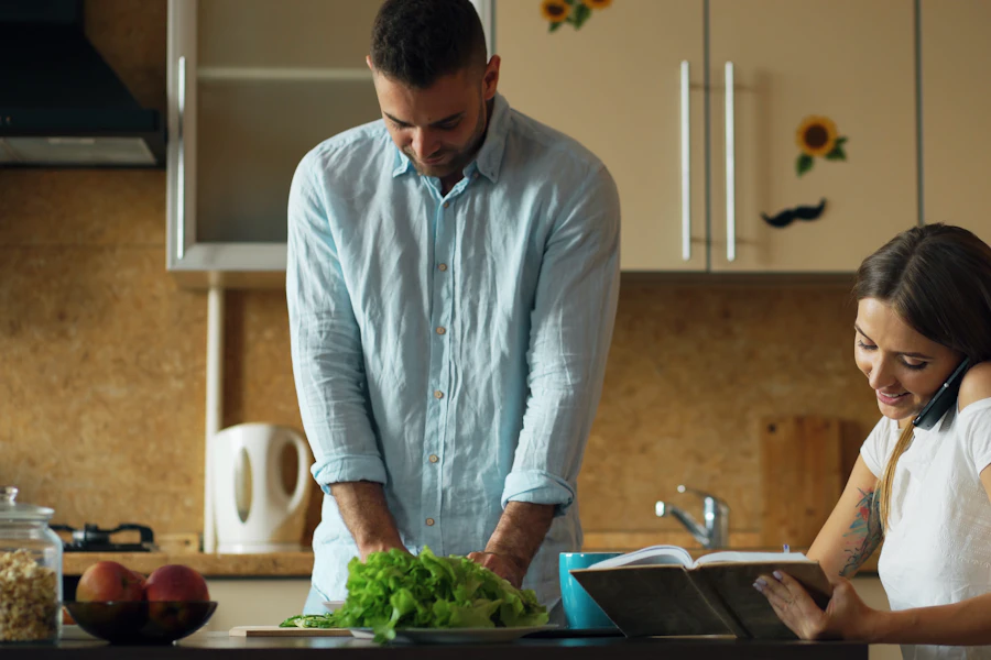 Two people cooking together, one checking a recipe while the other prepares ingredients